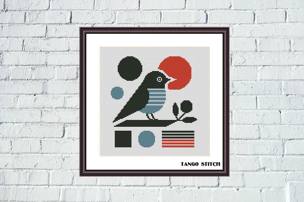Framed cross-stitch pattern of a bird on a branch with geometric shapes, displayed on a white brick wall. Abstract modern minimalist stripe bird cross stitch pattern - Tango Stitch