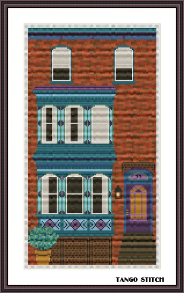 Cross-stitched depiction of a colorful building with windows and a door, framed by Tango Stitch.
