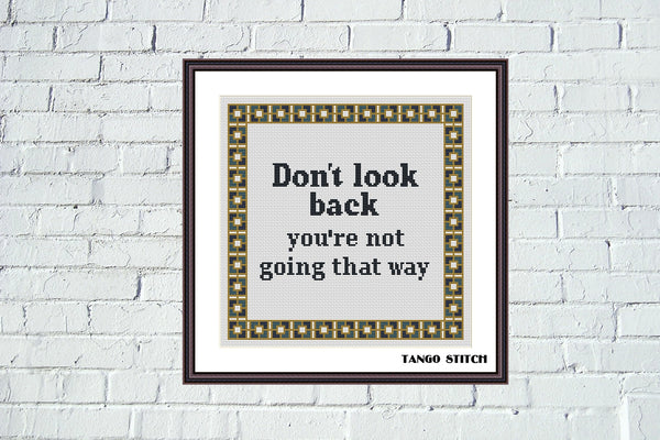 Framed print with motivational quote 'Don't look back, you're not going that way' on a white brick wall. Don't look back motivational cross stitch pattern - Tango Stitch