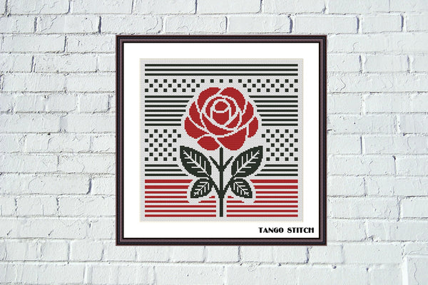 Framed artwork with a red rose design on a white brick wall. Red rose abstract geometric cross stitch pattern, Tango Stitch