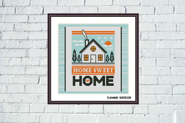 Framed artwork with 'Home Sweet Home' text and a house illustration on a white brick wall. Home card housewarming cross stitch pattern - Tango Stitch