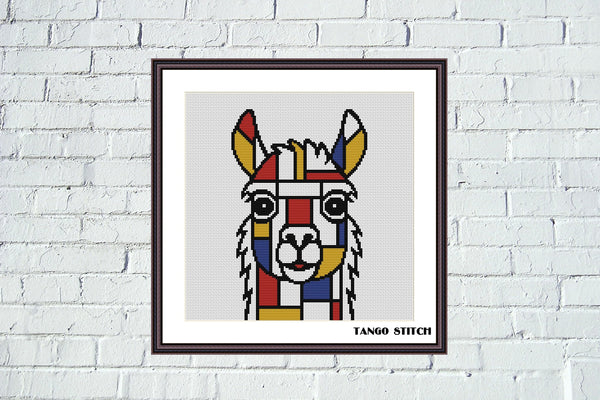 A framed cross-stitch art print of a stylized llama or alpaca face in a geometric, Piet Mondrian-inspired color block pattern, displayed on a white brick wall. The print features red, yellow, blue, green, and black blocks on a light gray stitched background, enclosed in a white mat and a dark brown frame. Mondrian Llama Geometric Alpaca Cross Stitch PDF Pattern - Tango Stitch
