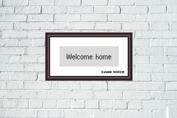Framed cross-stitch art with 'Welcome home' text on a white brick wall. Small size letters alphabet font cross stitch pattern - Tango Stitch