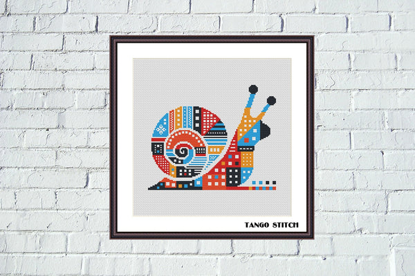 Framed artwork of a colorful snail design on a white brick wall. Modern Geometric Snail Cross Stitch Pattern- Tango Stitch